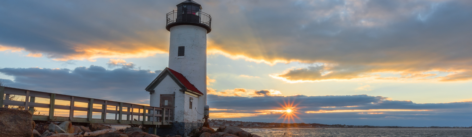 Annisquam Gloucester scenic photo of boardwalk to lighthouse with ocean view and sunset in background.