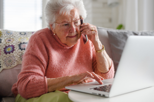 Concerned elderly woman on the phone in front of her laptop.