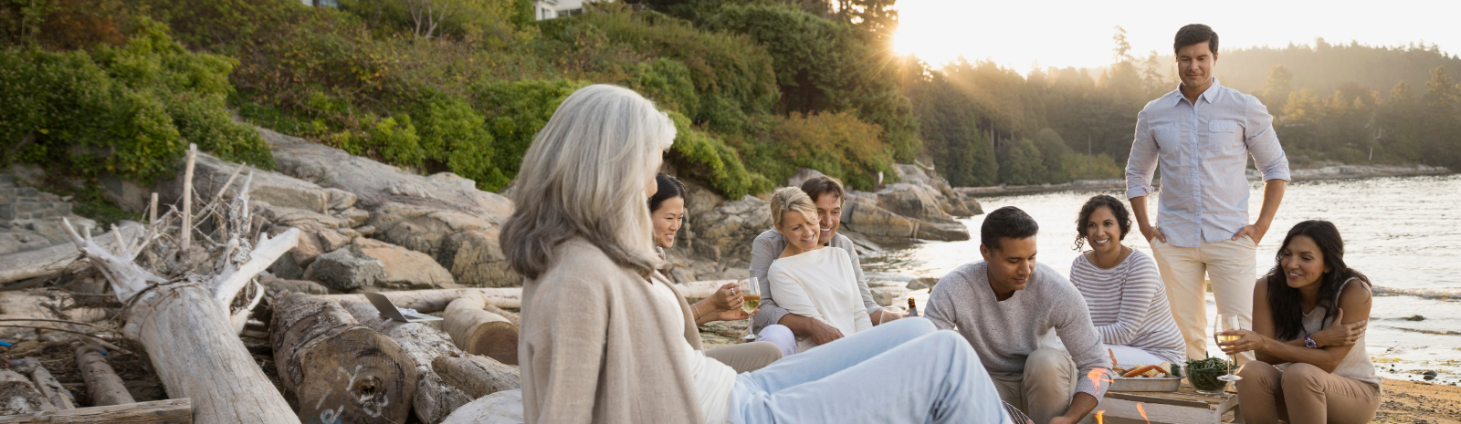 Group photo of people oceanside, sitting on the rocks in light colored clothing having a picnic.