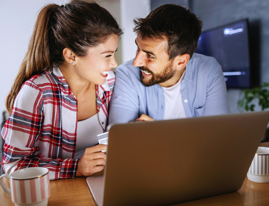 Young couple looking at each other smiling in front of a laptop with a debit card in hand.