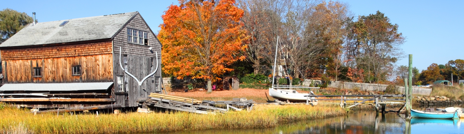 Scenic photo of Essex, a big wooden barn with a dock and boats in and out of the water, on the shoreline of a body of water.