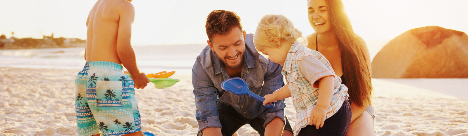 Family photo of a man and woman with two young boys playing in the sand on the beach.