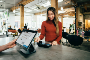 Woman in red sweater in front of register, swiping her card to pay.
