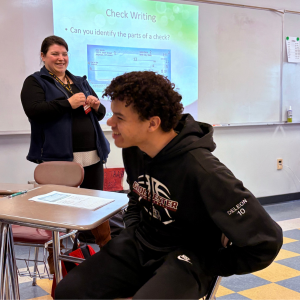 Gloucester branch manager Britney Tarantino performing presentation at local Gloucester High School about how to write checks. Photo of Britney and young male student both smiling as she presents.