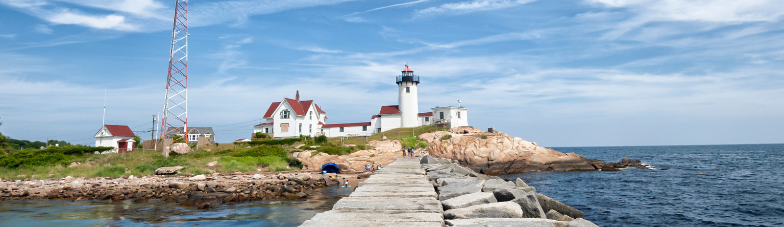 Scenic photo of Gloucester, on the breakwater, focusing on the white and red lighthouse building.